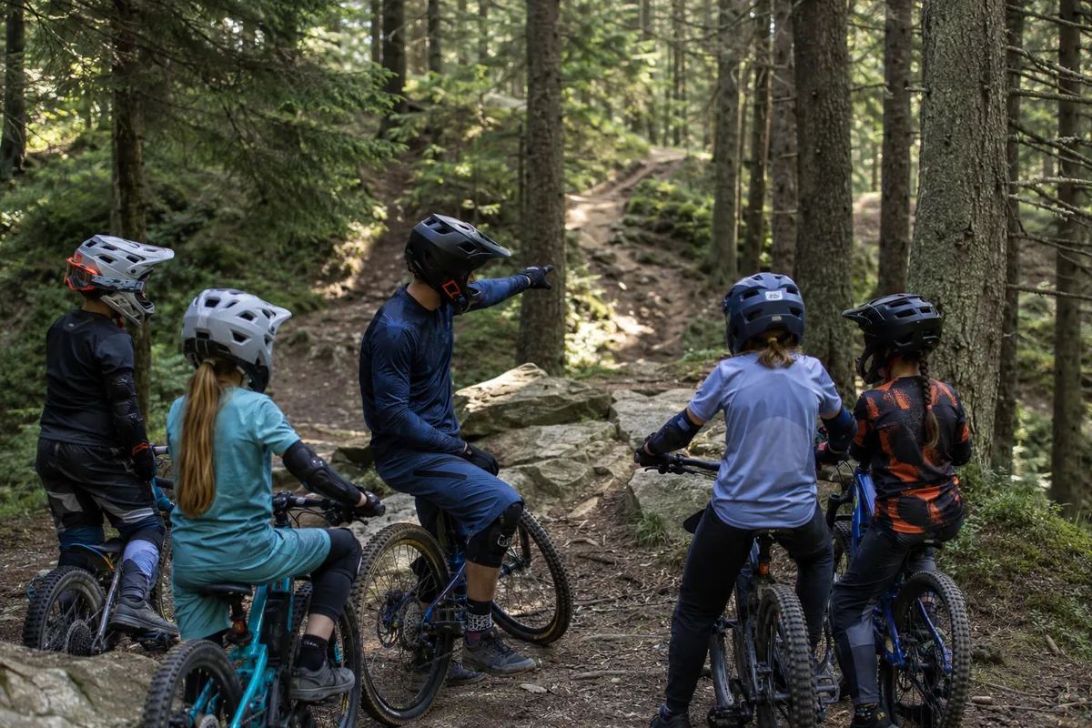 Trener pokazuje dzieciom linię przejazdu na leśnej trasie MTB